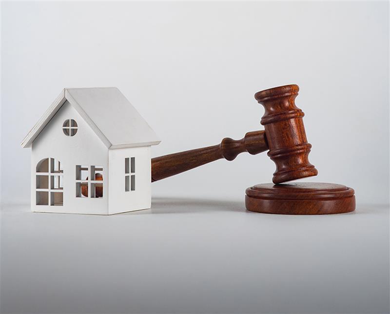 Wooden judge's gavel resting against a small model house, symbolizing property law and legal verification in real estate.